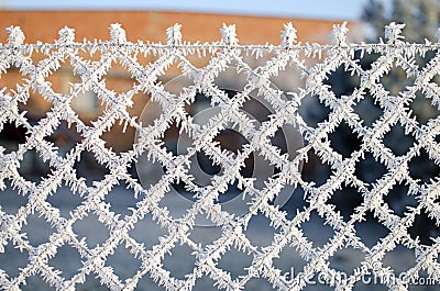 Close-up view of a wire fence with frost with ice crystals under a blue sky with a blurred background Stock Photo