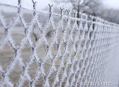 Close-up view of a wire fence with frost with ice crystals under a blue sky with a blurred background Stock Photo