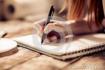 Close up view of womans hand writing with pen on notebook on wooden table. Stock Photo