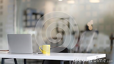 Close up view of workplace with tablet, office supplies and yellow coffee cup on white table with blurred office room Stock Photo