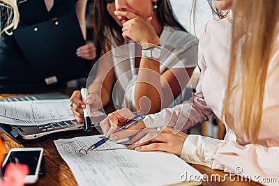 Close-up view of young women working on accounting paperwork checking and pointing at documents sitting at desk in Stock Photo