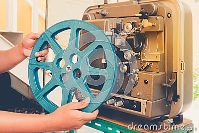 Close up of vintage classic mobile 8 mm or 16 mm movie film projector and hand holding empty film reel with vintage color style. Stock Photo