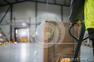 Close up of warehouse worker maneuvering pallet jack loaded with goods through the warehouse. Stock Photo