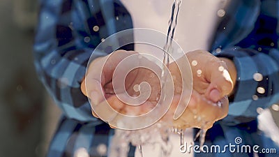 Close-up of water splashes pouring on the hands of a person, washing palms in the reflective glare of the sun, wet drops Stock Photo