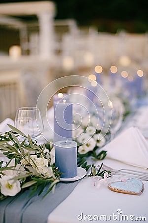 Close-up of a wedding dinner table at reception. Blue thick candles burn on the table among floral arrangements of white Stock Photo