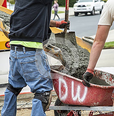 Close up of Wet cement off loaded by construction workers using a shovel from a cement truck chute into a wheelbarrow Stock Photo