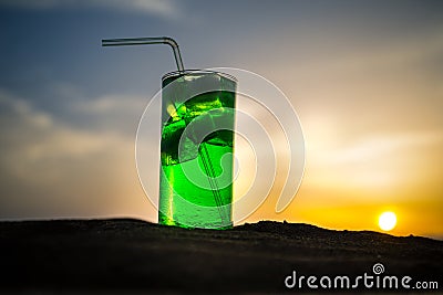 Close up wet glass of green cold mint drink, colorful orange sunset background on the terrace. Cooling summer drink. Summer fresh Stock Photo