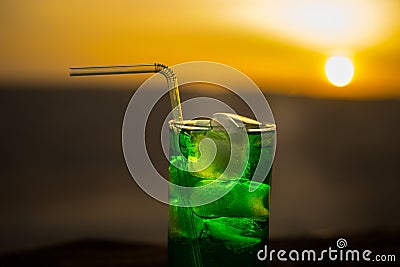 Close up wet glass of green cold mint drink, colorful orange sunset background on the terrace. Cooling summer drink. Summer fresh Stock Photo