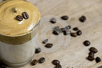 Close up of whipped instant coffee on a cup of milk on a crystal glass with coffee beans on a wooden surface. Dalgona coffee Stock Photo