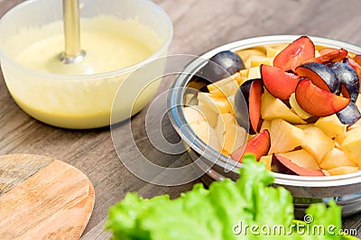 Close-up of whipping a mixture of homemade mayonnaise with a blender in a plastic bowl. Sliced apples and plums in a Stock Photo