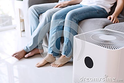 Close up of white air purifier on the floor in living room the background of young Asian couple relaxes on sofa. Concept of caring Stock Photo
