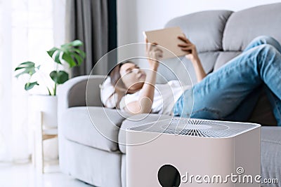 Close up of white air purifier on the floor in living room the background of young Asian woman relaxes. Concept of caring for Stock Photo