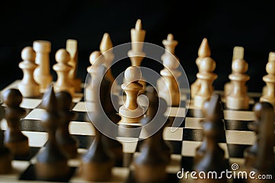 Close up of white and black chess pieces on board. Selective focus on first move of white pawn on chessboard. Concept of Stock Photo