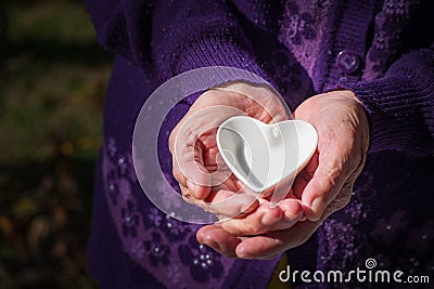 Close-up of a white ceramic heart-shaped on palm senior woman. Valentine`s day. Concept of aged people and healthcare Stock Photo