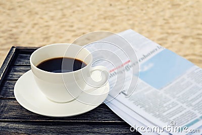 Close up white coffee cup on wood table at sunrise sand beach with newspaper in the morning, warm tone Stock Photo