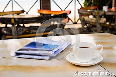 Close up white coffee cup on yellow table at sunrise sand beach with newspaper in the morning Stock Photo