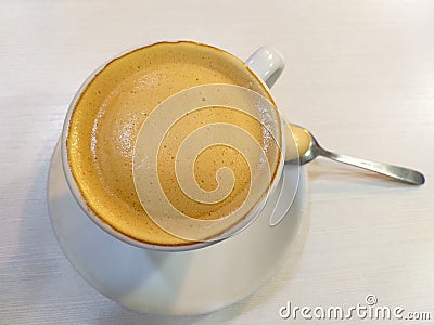 white cup of coffee with milk a metallic teaspoon on a white saucer on a white table Stock Photo