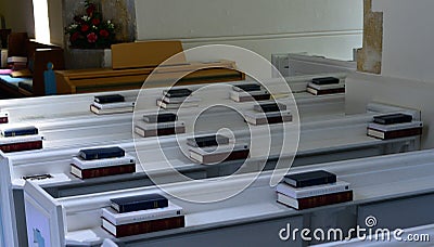 close up of white painted pews in a small English church with hymn books neatly stacked Stock Photo