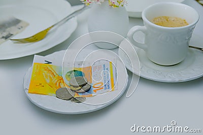 Close-up of white plate for money, Swiss francs banknotes and coins, Restaurant bill, cup of coffee, delicate pink flowers, dishes Stock Photo
