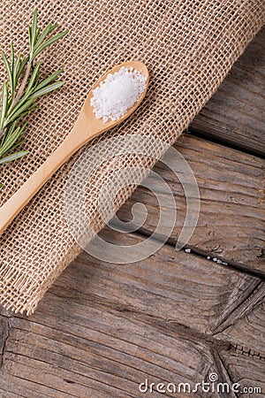 Close-up of white rock salt in wooden spoon by rosemary on jute fabric at table Stock Photo