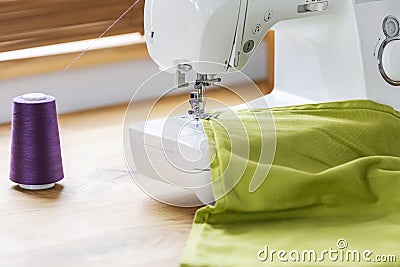 Close-up of a white sewing machine stitching a purple thread on a green fabric in a crafts room interior. Real photo. Stock Photo