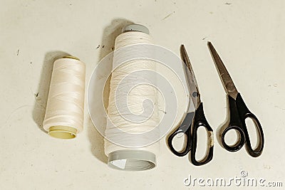 Close-up of a white table surface with a pair of scissors, tow spool of thread Stock Photo