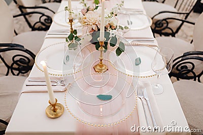 Wedding dinner table reception. Close-up of wildcard with gold beads, transparent glass. Runner of pink silk. Candles in Stock Photo