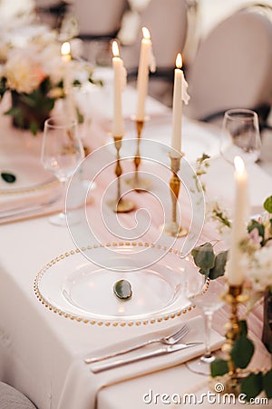 Wedding dinner table reception. Close-up of wildcard with gold beads, transparent glass. Runner of pink silk. Candles in Stock Photo