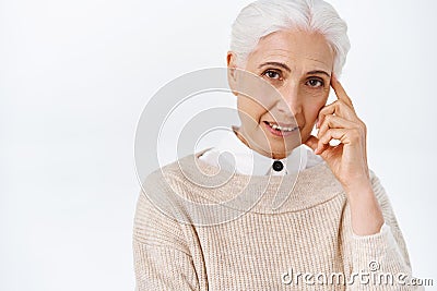 Close-up wise old lady with grey hair teaching kids important lesson, touching temple with finger to tell think before Stock Photo