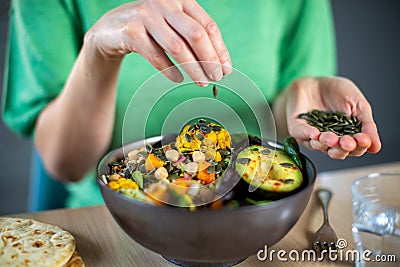 Close Up Of Woman Adding Pumpkin Seeds To Healthy Vegan Meal In Bowl Stock Photo