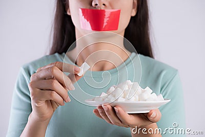 Close up woman beautiful hands holding white sugar cubes and close mouth by red tape. Healthcare concept Stock Photo