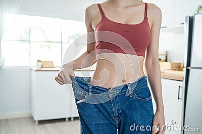 Close up of woman feel happy after lose weight for health in house. Attractive beautiful skinny girl wearing old big jeans with Stock Photo