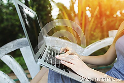 Close up woman hand fingers press laptop keyboard for remote work on sunny day, background of sunshine green palms in Stock Photo