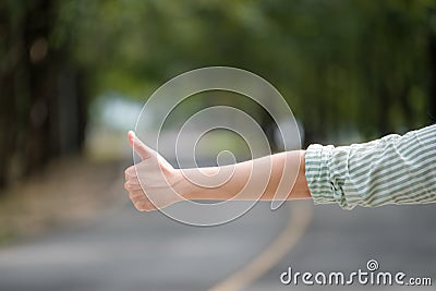 Close up woman hand hitchhiking at countryside road near forest,Alone travel or single traveller or hitchhiker concept Stock Photo