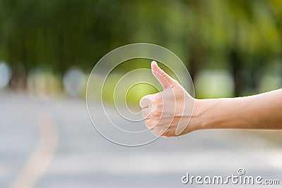 Close up woman hand hitchhiking at countryside road near forest,Alone travel or single traveller or hitchhiker concept Stock Photo