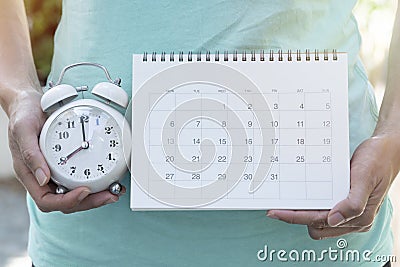 Woman hand holding calendar and alarm clock for planner, business, check for period schedule, healthy and travel plan Stock Photo