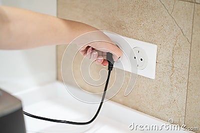 Close up Woman hand insert or pull out elecrticity plug in outlet on the wall Stock Photo