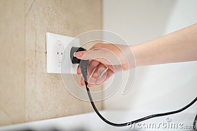 Close up Woman hand insert or pull out elecrticity plug in outlet on the wall Stock Photo