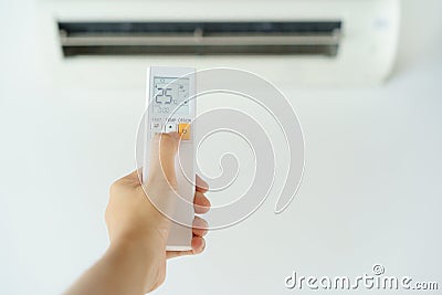 Close-up woman hand operating air conditioner with remote control. Open air conditioning 25 degrees Stock Photo