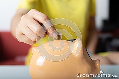 Close up woman right hand putting one coin into piggy bank Stock Photo