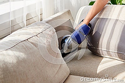 Close up of woman hand with vacuum cleaner, copy space. Woman cleaning sofa with vacuum cleaner. Household and spring-cleanig. Stock Photo