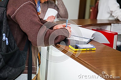 Close up of a woman hand writing or signing in a document on a reception zone of clinic. Selective focus Stock Photo