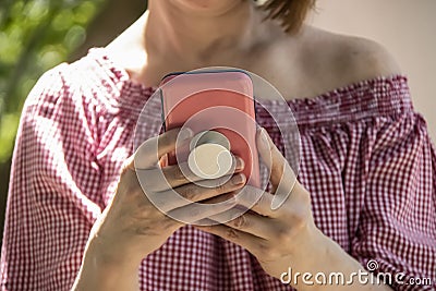 Close-up of woman holding and reading from a cell phone in pink case with grip handle on back - off shoulder blouse and short Editorial Stock Photo