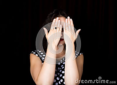Close-up woman looks straight into the camera on a black background. laughing woman covering her eyes with her hand Stock Photo