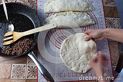 Close up of a woman`s hands making dough for homemade bread on a silicone baking sheet. frying pan with grinned meat on the side Stock Photo