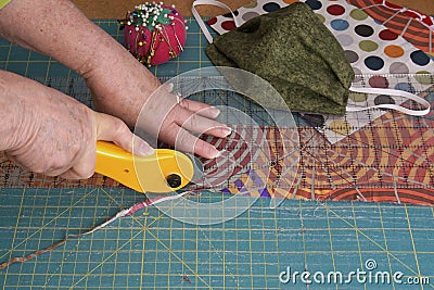 Close-up of a woman`s hands using a rotary cutter to cut leftover quilting fabric for hand sewn face masks Stock Photo