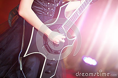 Close-up of a woman on stage playing on electro guitar. The girl rockstar in a black dress Stock Photo