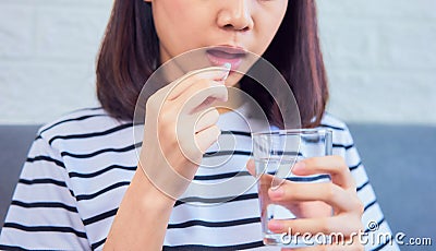 Close up of woman taking white pill in mouth and drinking water in glass on sofa in house, feels like sick. Health care concept. Stock Photo