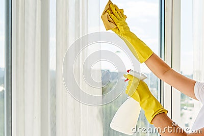 Close up of woman in yellow rubber gloves cleaning window with cleanser spray and yellow rag at home or office, copy space. Stock Photo