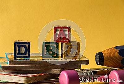 Closeup of Woodblock letters a, b, c, d, children reading books, big yellow and blue pencils in front of a yellow background. Stock Photo